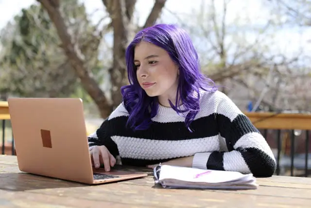 Student with purple hear wearing a stripped sweater looking at her laptop